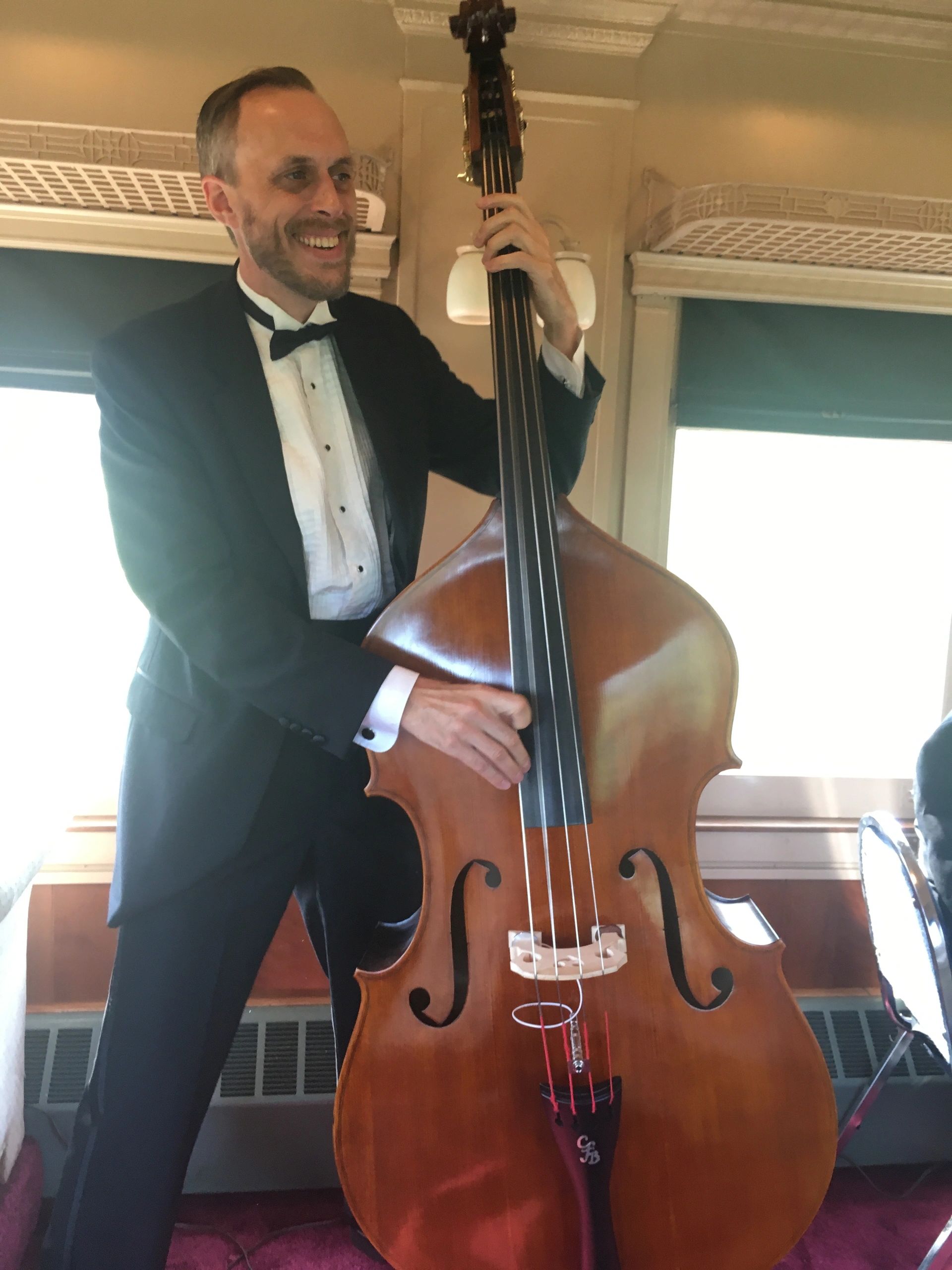 Matt Senjem in a tuxedo playing upright bass in a vintage rail car